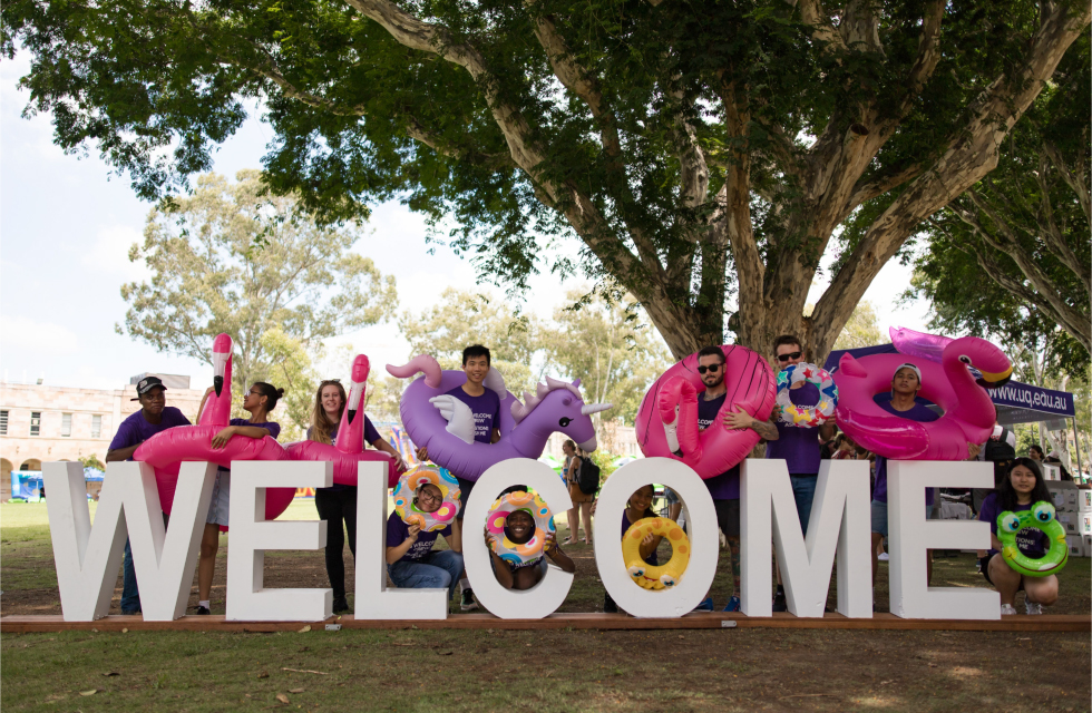 Students smiling, standing with large welcome sign. 