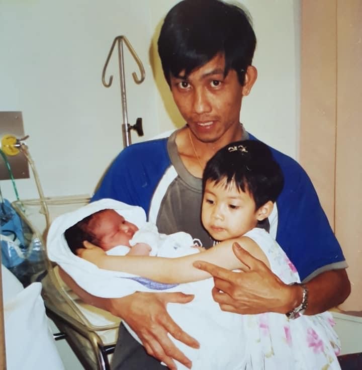 A Vietnamese man holds a newborn baby and a young girl. 