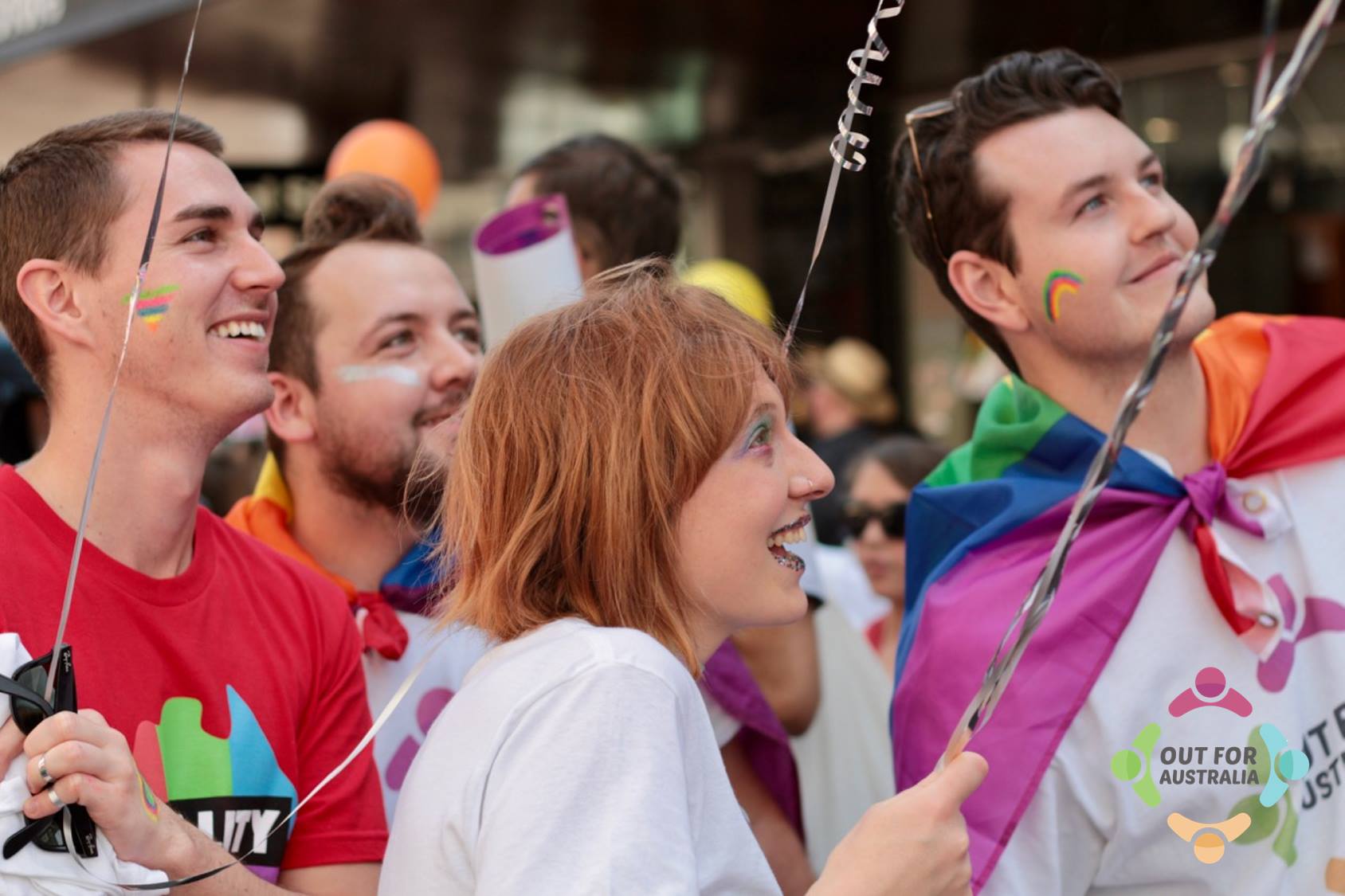 students posing in rainbow flags as a marriaege equality march looking up