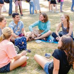 7 students sitting in a circle on the grass chatting