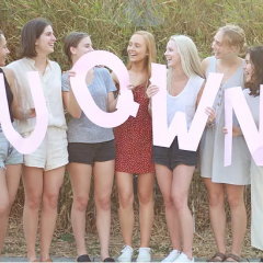 7 women posing with paper letters "U Q W N" 